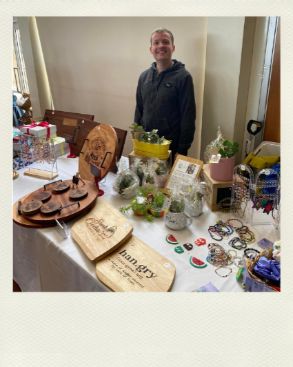 Jessie smiling proudly behind a market table of microenterprise products.