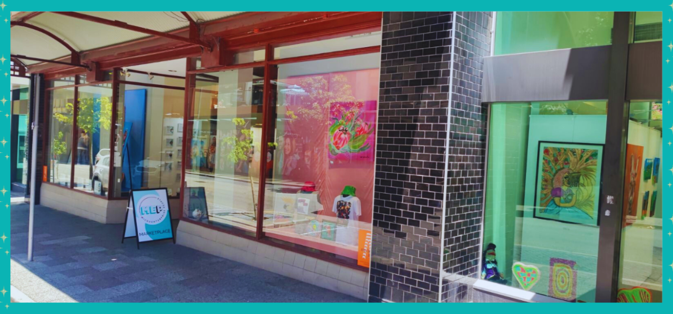 A storefront displaying bright and colorful microenterprise creations in the windows. There is a MEP a-frame sign in the doorway.