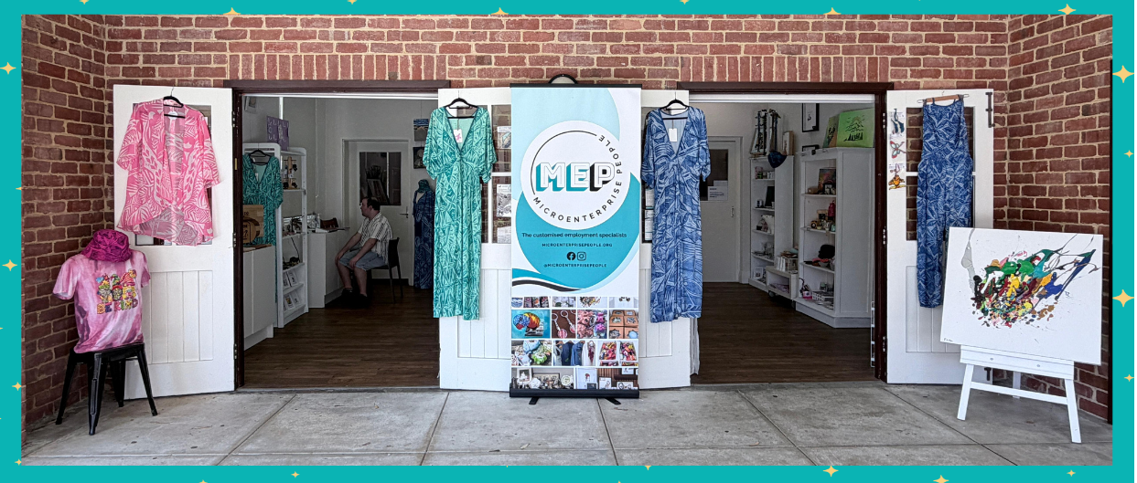 A storefront displaying bright and colorful microenterprise creations hanging on two entry door frames. There is a MEP sign in between the doorways.
